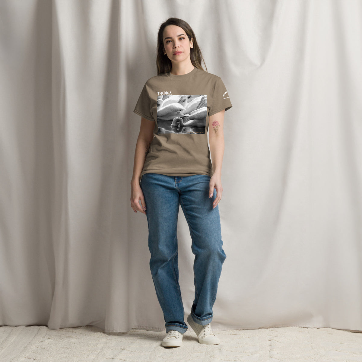 A woman modeling a light brown graphic t-shirt with a black and white photo of pelicans feeding on the water